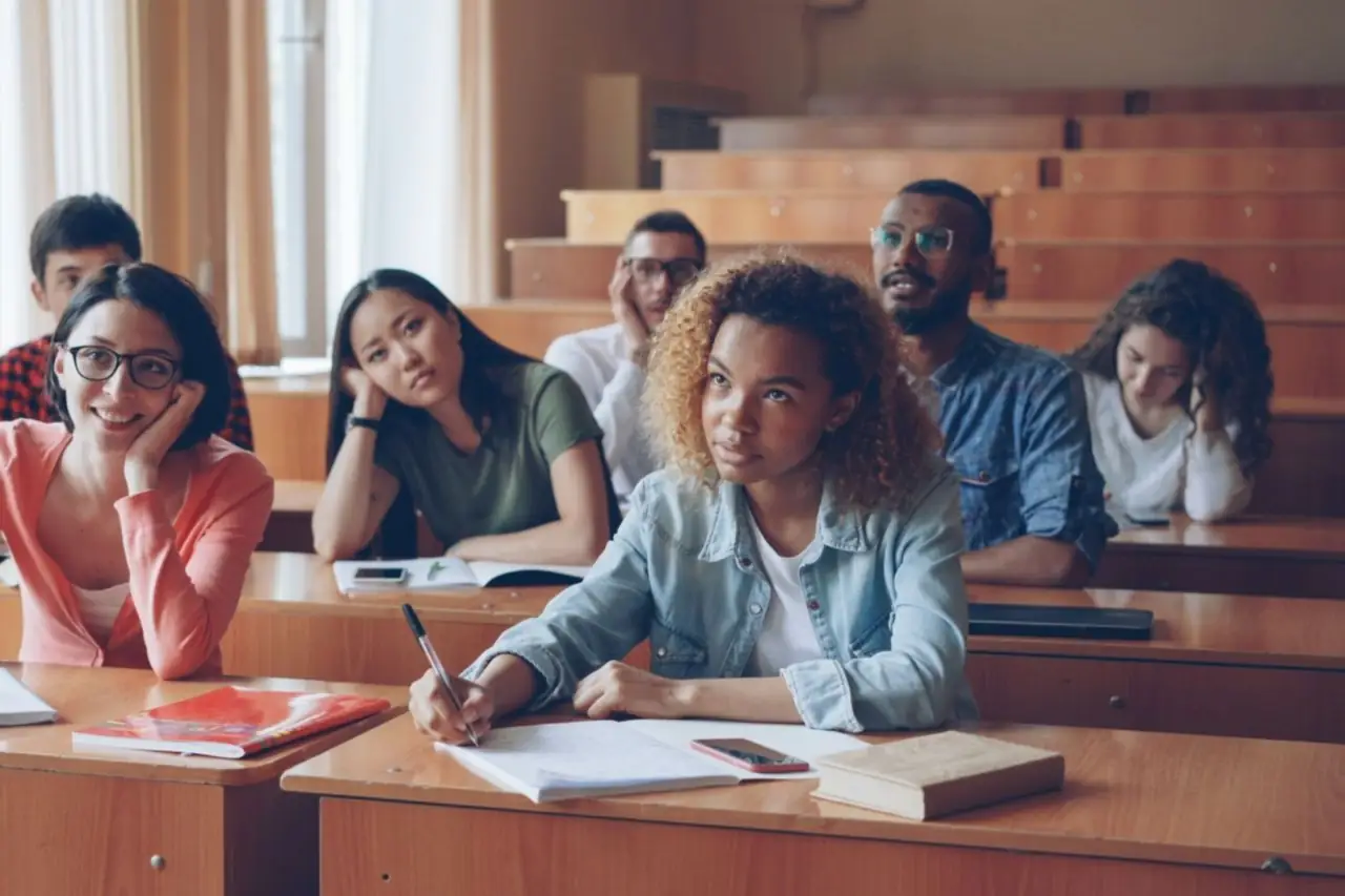 Étudiantes et étudiants attentifs, cahiers ouverts, sur les bancs en bois d'un amphithéâtre